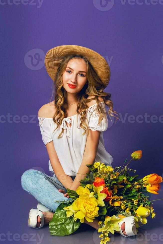 studio moda ritratto di bella carino bionda donna nel cannuccia cappello, bianca cotone camicia seduta e Tenere mazzo di sorprendente primavera fiori. indossare elegante retrò attrezzatura . foto