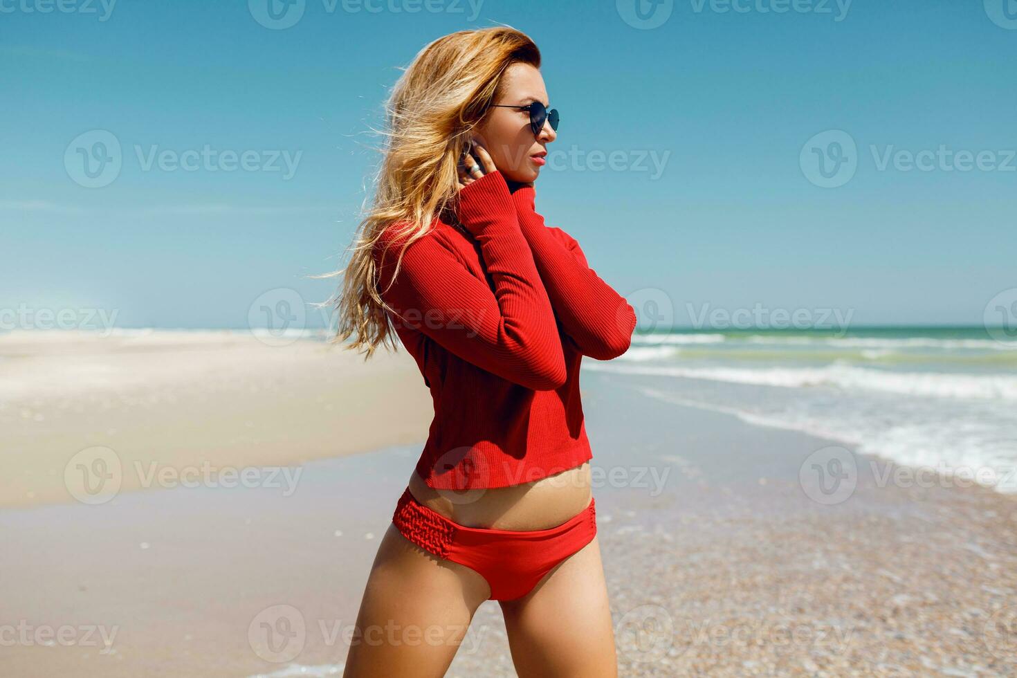 vacanze e viaggio concetto. Meraviglia biondo donna guardare su il oceano. indossare sexy rosso bikini. vuoto spiaggia. tropicale isola. Perfetto figura. foto