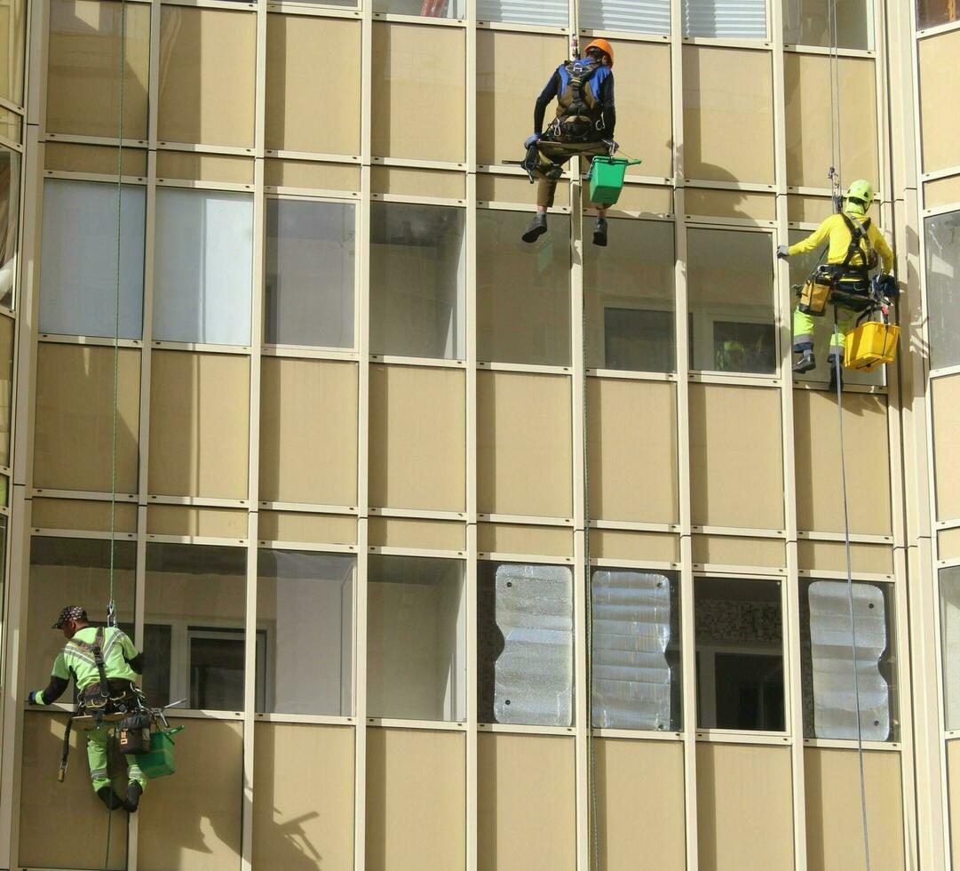 sankt petersburg Russia - 10 12 2023 tre industriale scalatori a partire dal il pulizia servizio lavare il bicchiere facciata di un' moderno grattacielo appartamento costruzione. corda accesso foto