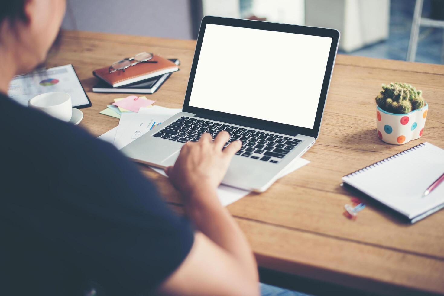 le mani dell'uomo che digitano lavorando con il computer portatile sulla scrivania in legno foto