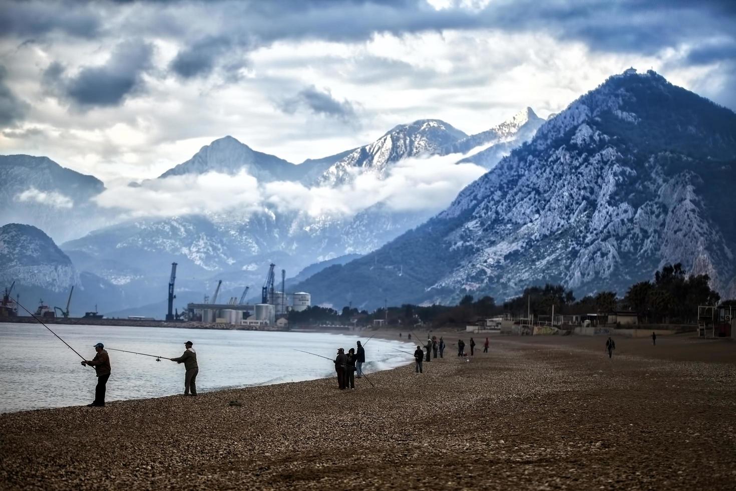 montagne nuvole e persone che pescano vicino al mare foto