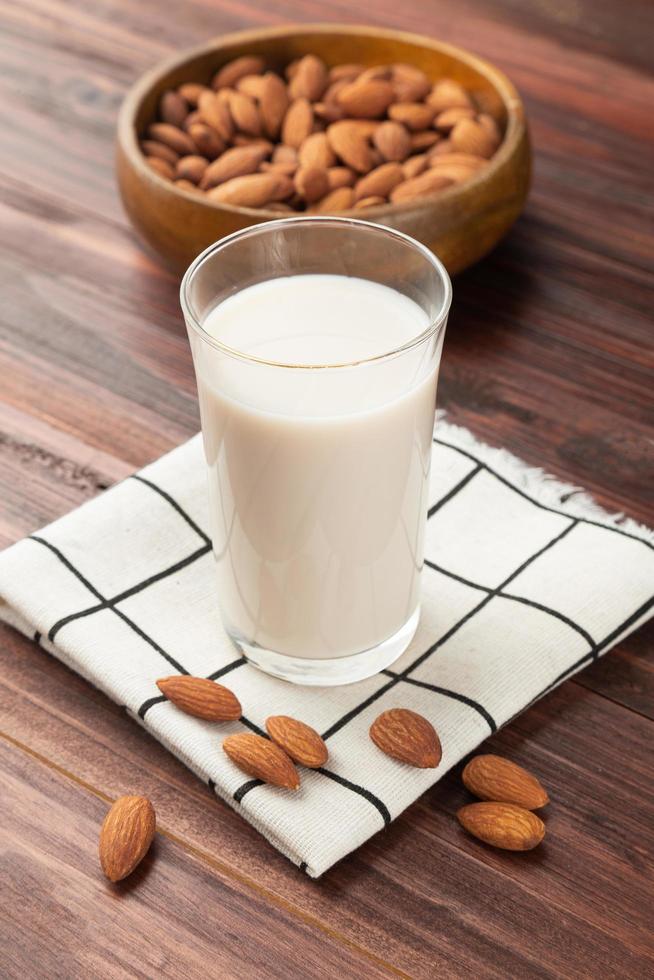 latte di mandorla nel bicchiere con mandorle in ciotola di legno sul tavolo foto