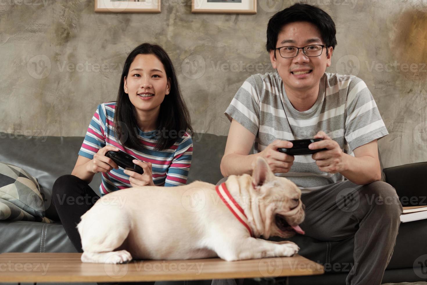 la coppia asiatica sta giocando ai videogiochi e al cane da compagnia nelle vicinanze. foto
