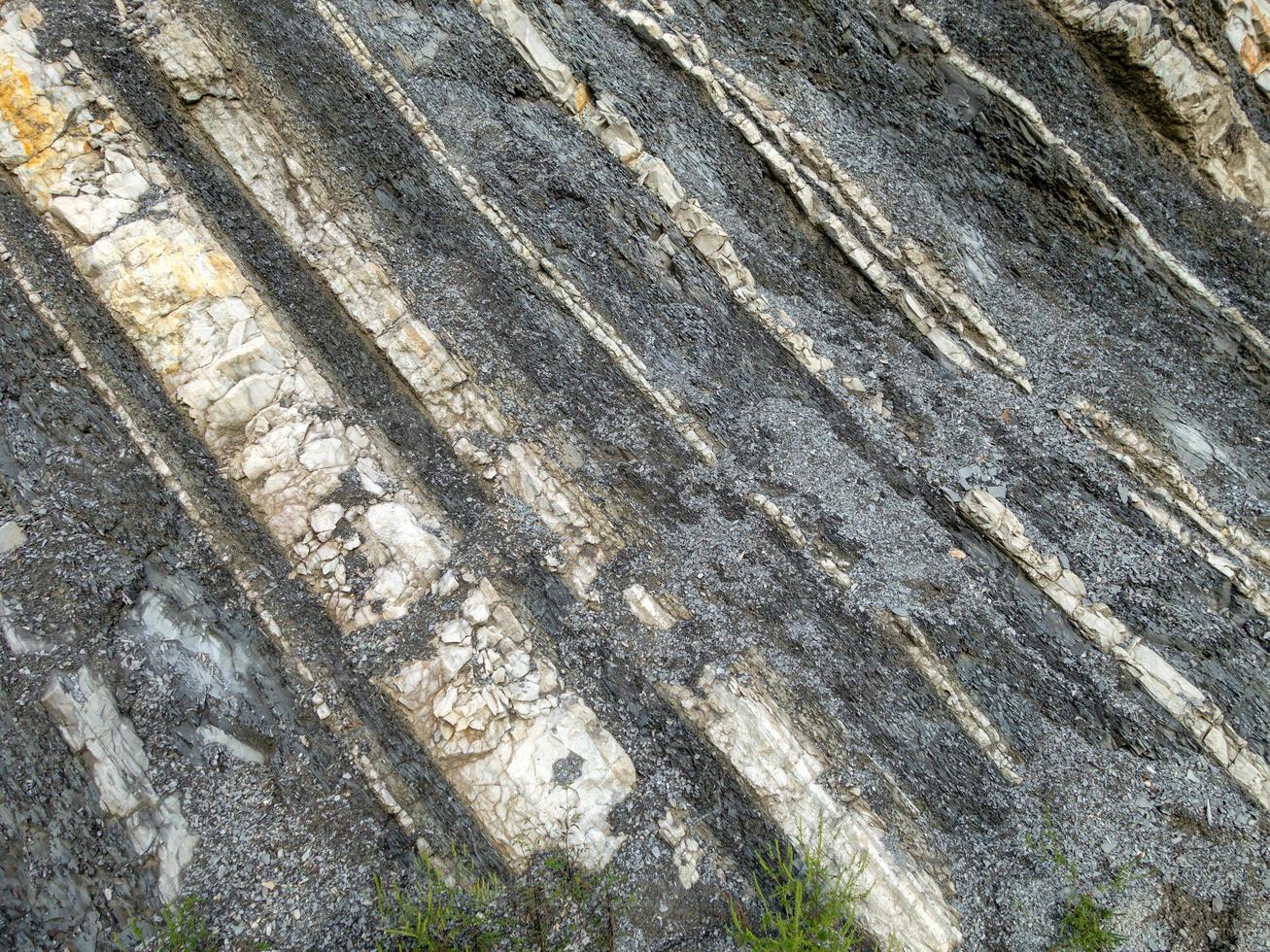 roccia di montagna di pietre di colore grigio, bianco, marrone a strati diagonalmente foto