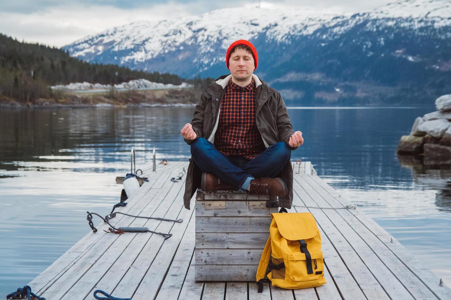 uomo viaggiatore in una posa meditativa su un molo sullo sfondo della montagna foto