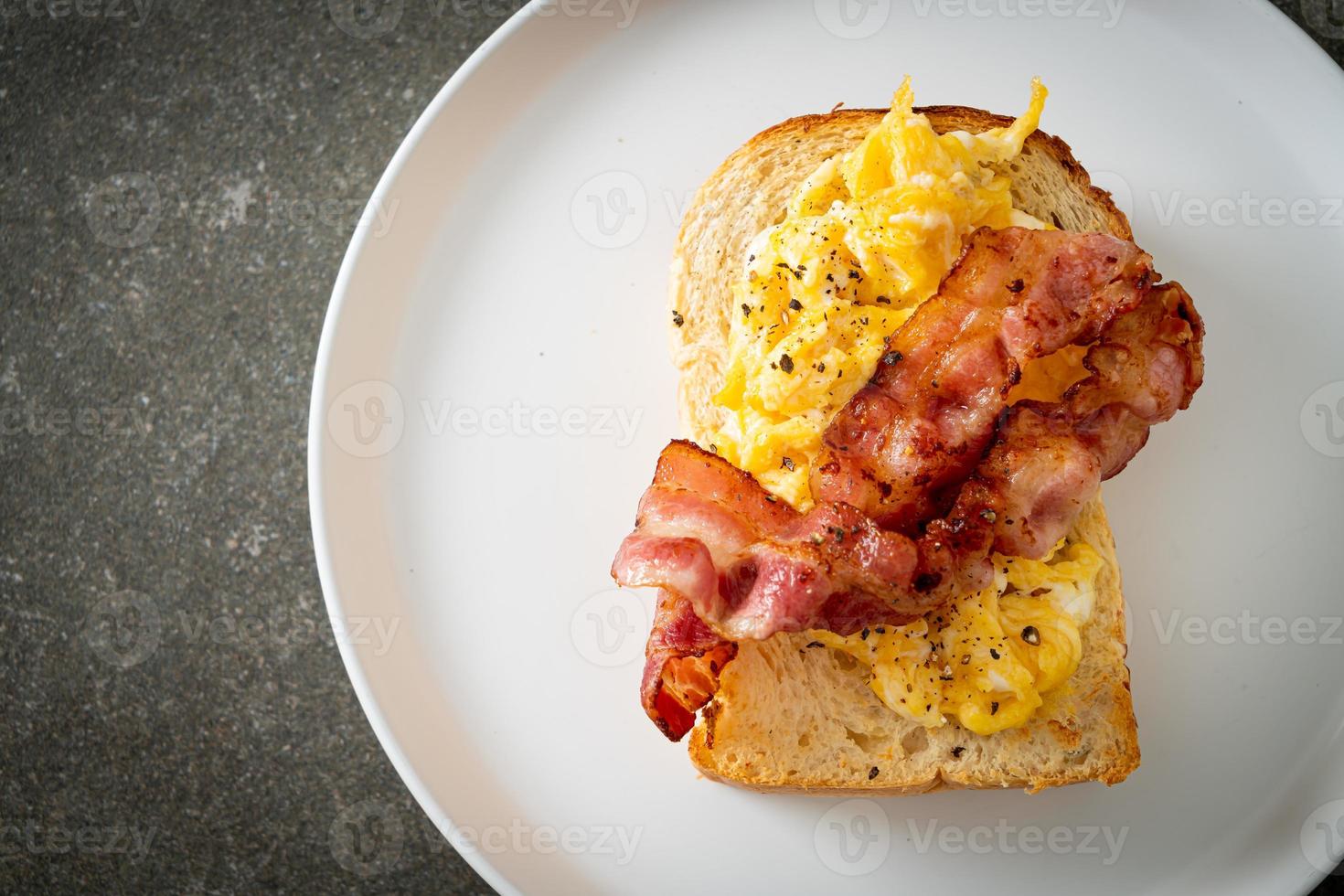 pane tostato con uova strapazzate e pancetta su piatto bianco foto