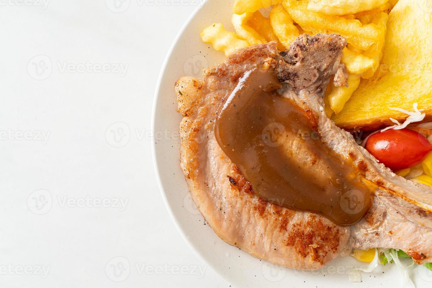 bistecca di braciola di maiale con patatine e mini insalata su piatto bianco foto