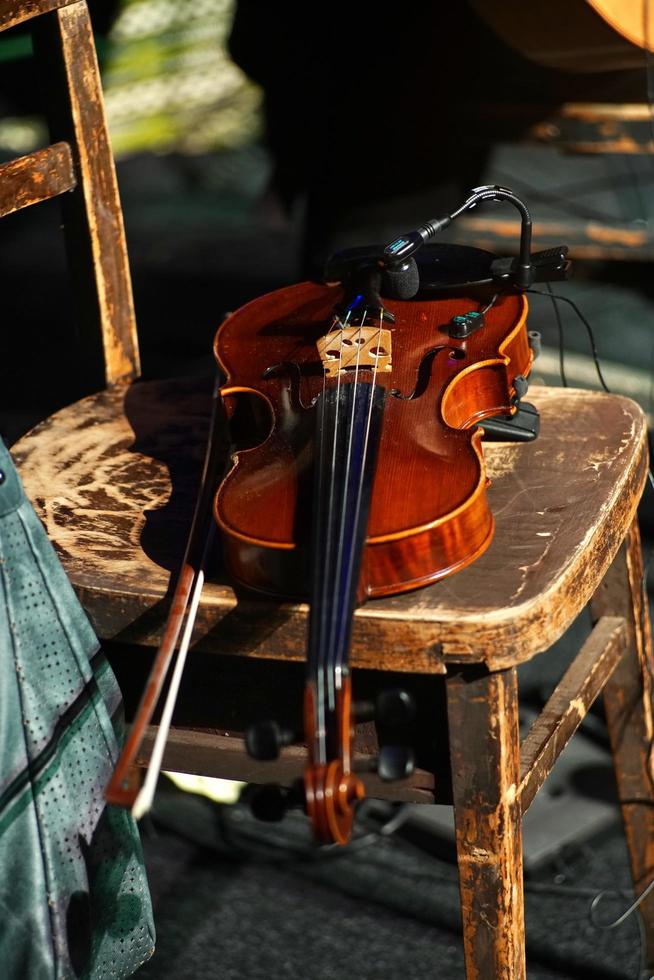 primo piano di un violino con un arco su una sedia di legno alla luce del sole foto