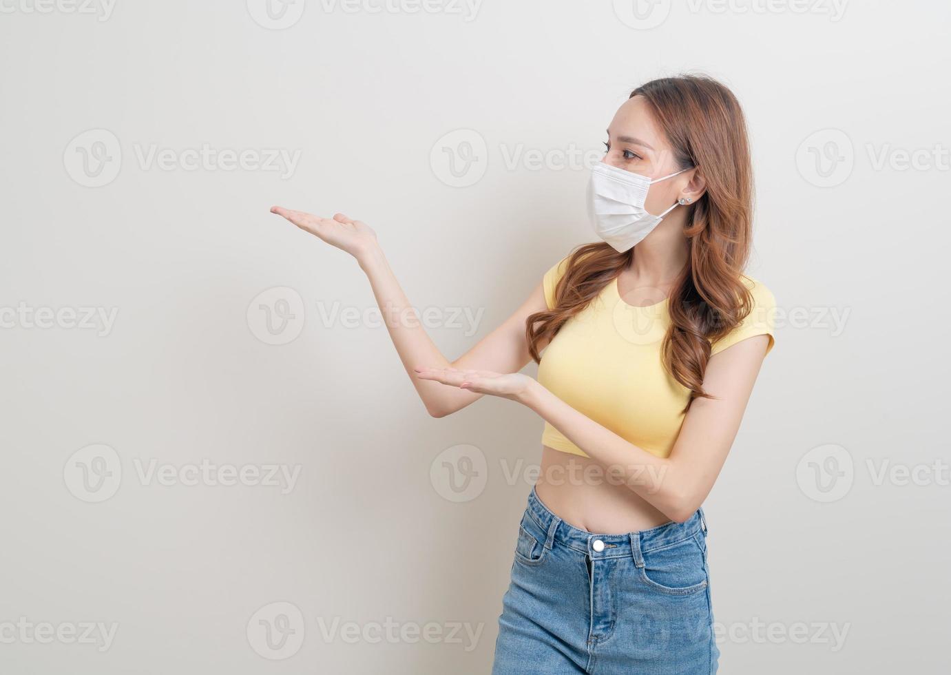 ritratto bella donna asiatica che indossa maschera con la mano che presenta o indica su sfondo bianco foto