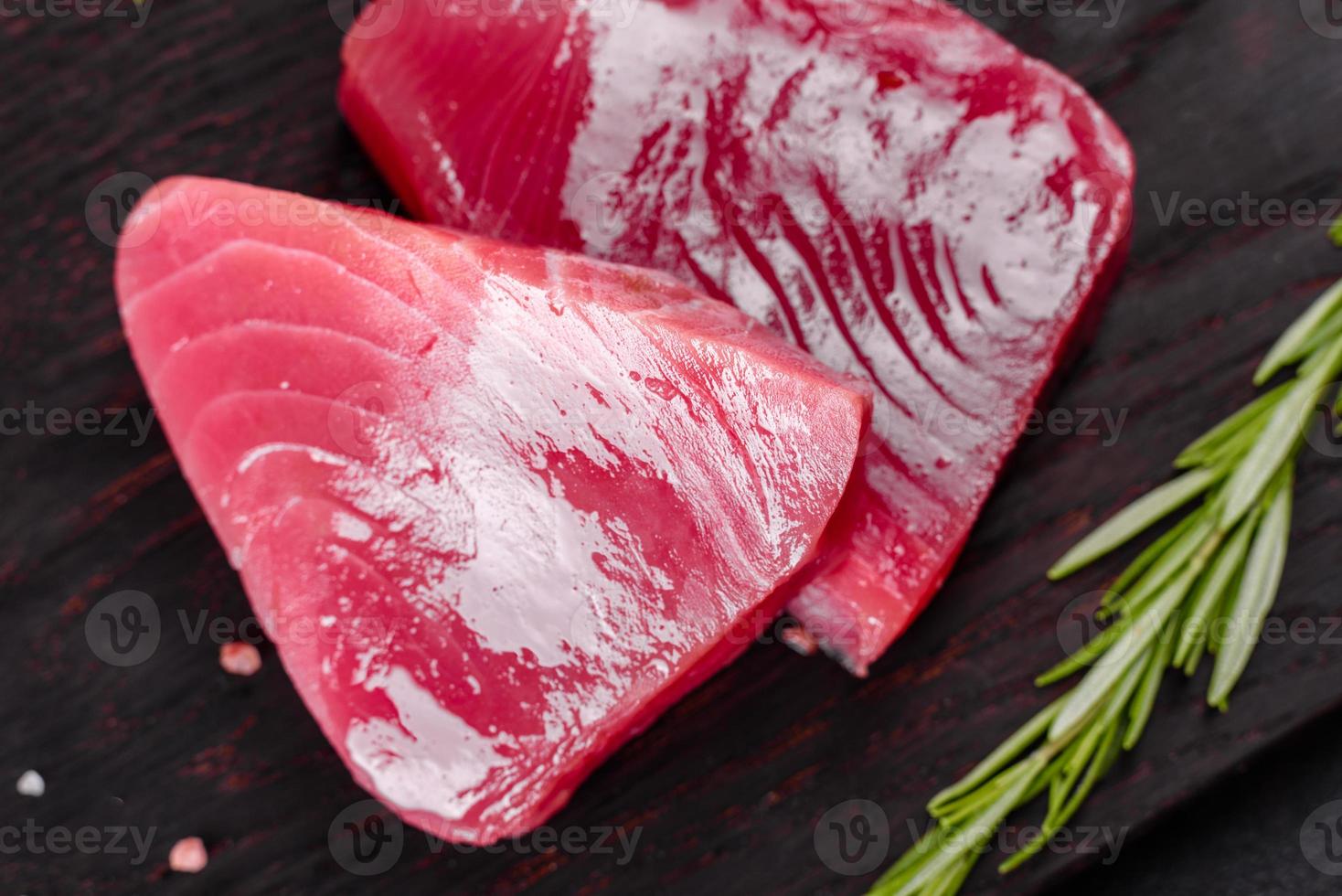 Bistecche di filetto di tonno fresco con spezie ed erbe aromatiche su sfondo nero foto