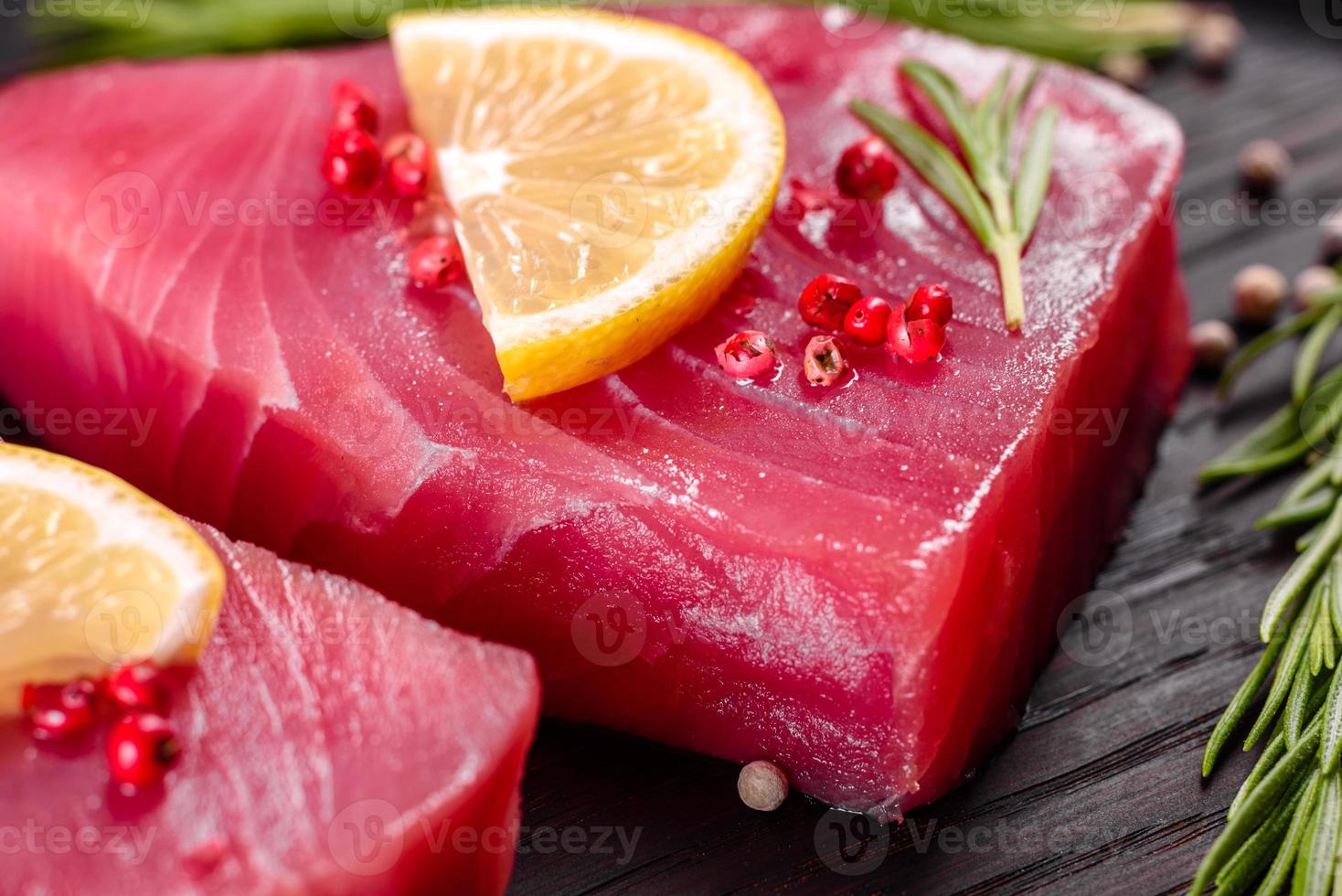 Bistecche di filetto di tonno fresco con spezie ed erbe aromatiche su sfondo nero foto