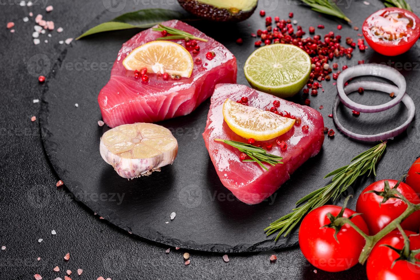 Bistecche di filetto di tonno fresco con spezie ed erbe aromatiche su sfondo nero foto