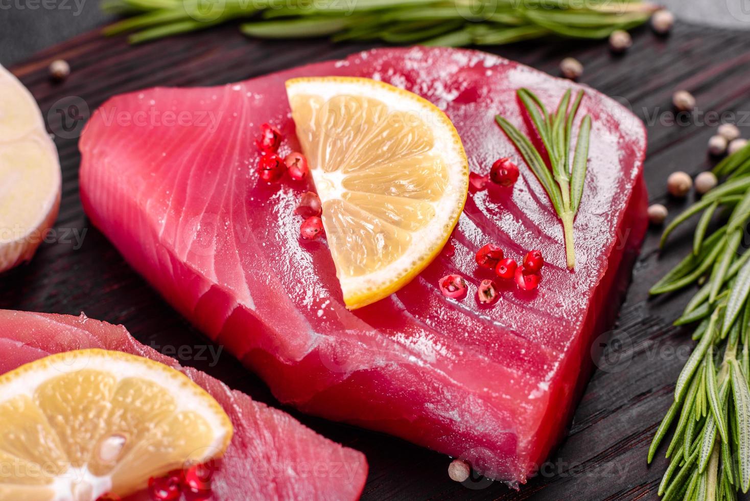 Bistecche di filetto di tonno fresco con spezie ed erbe aromatiche su sfondo nero foto