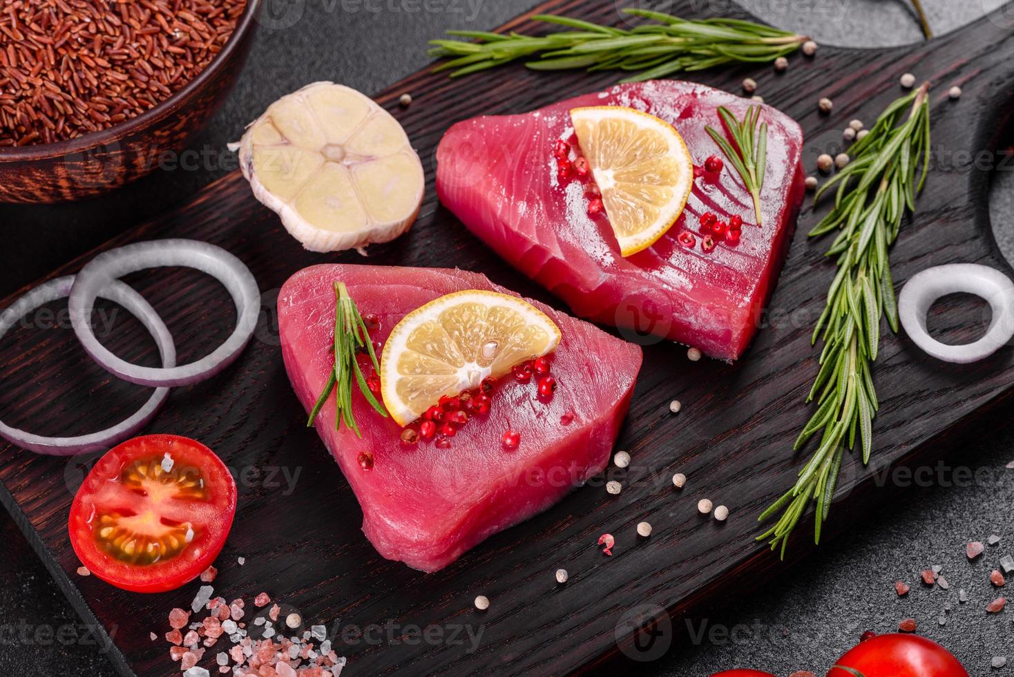 Bistecche di filetto di tonno fresco con spezie ed erbe aromatiche su sfondo nero foto