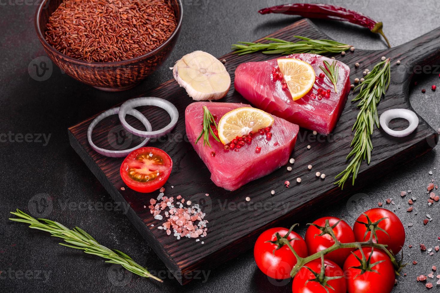 Bistecche di filetto di tonno fresco con spezie ed erbe aromatiche su sfondo nero foto