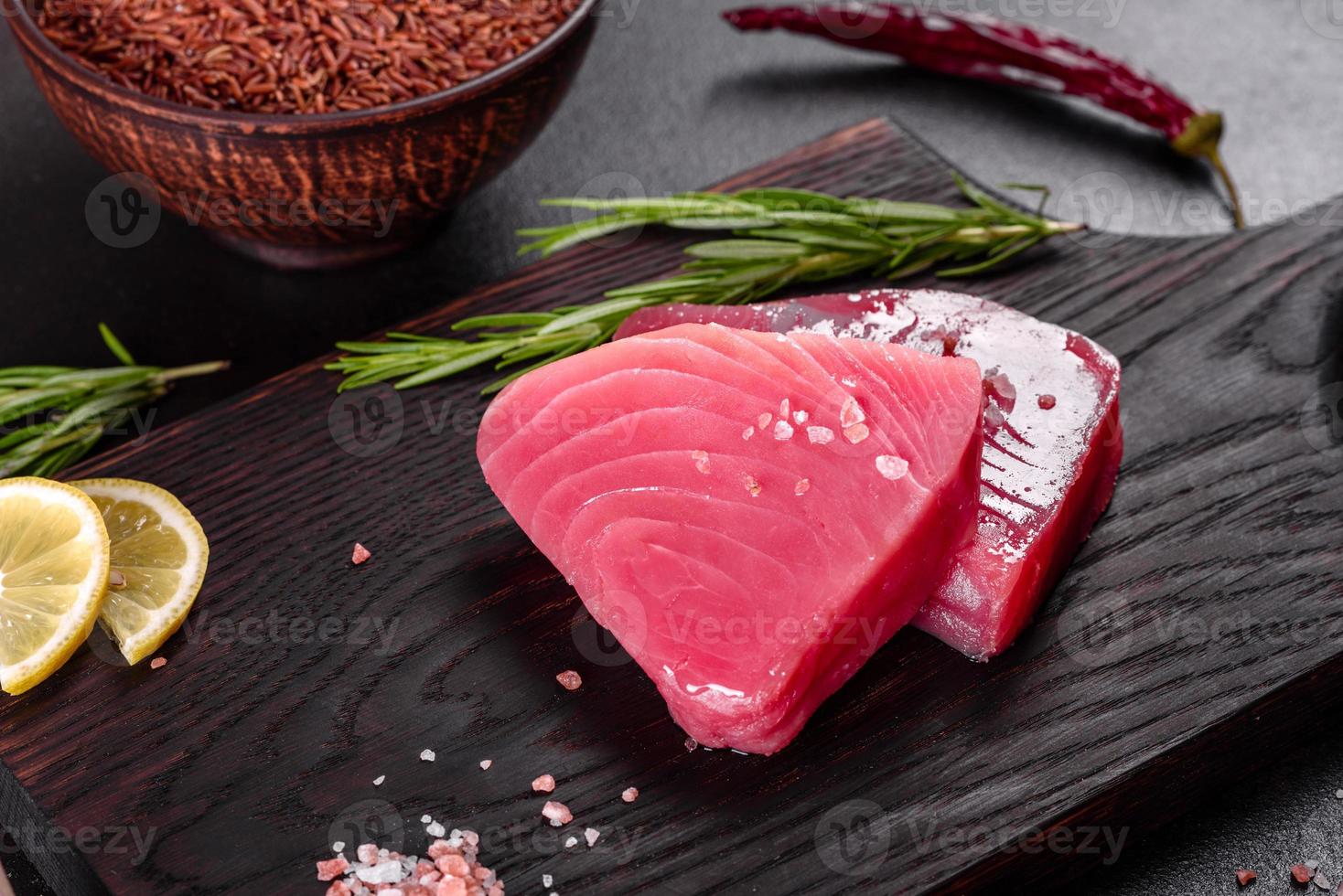 Bistecche di filetto di tonno fresco con spezie ed erbe aromatiche su sfondo nero foto