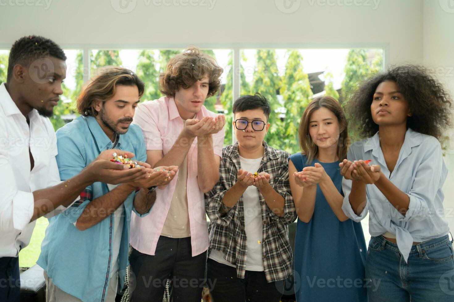 gruppo di multietnico amici avendo divertimento a festa giocando divertimento soffiaggio colorato carta foto