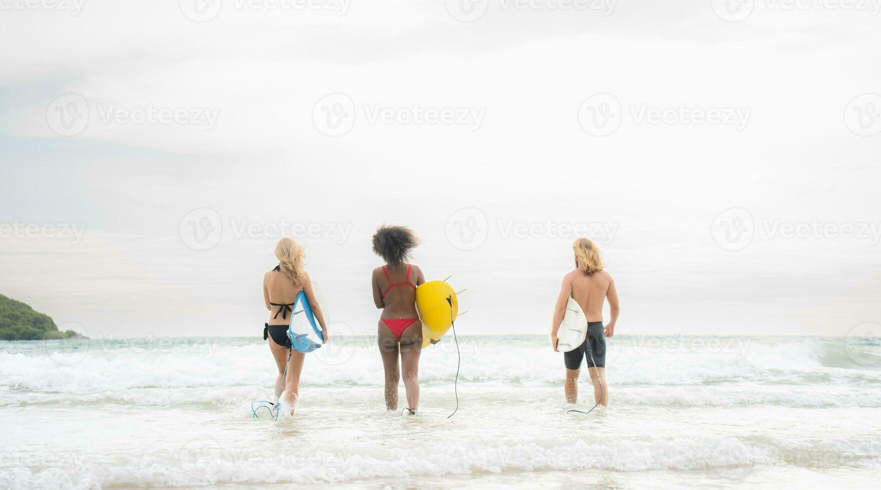 Due donne e giovane uomo Tenere tavole da surf pronto per camminare in il mare per Surf. foto