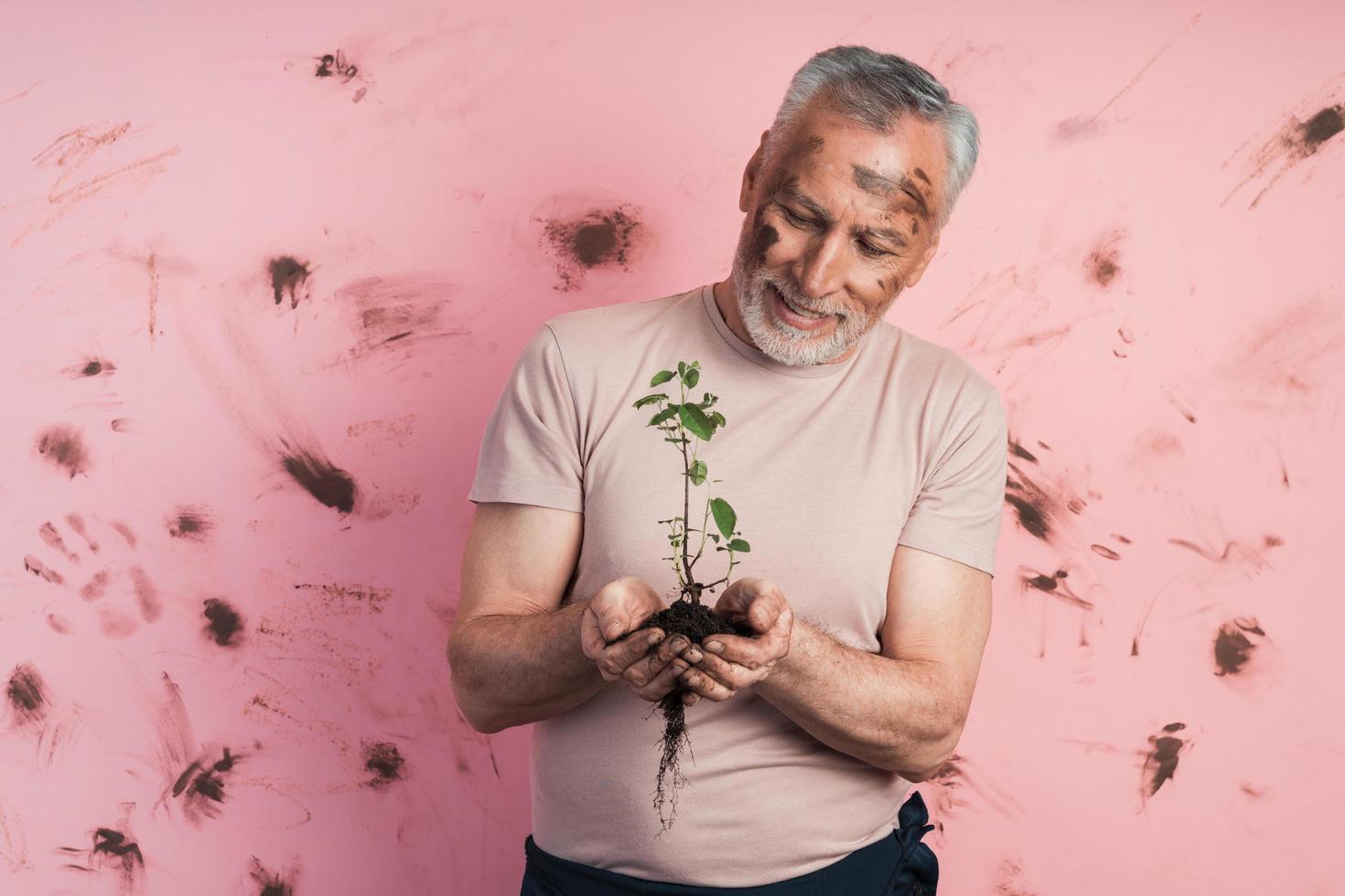 uomo anziano con i capelli grigi con la barba tiene una pianta tra le mani foto