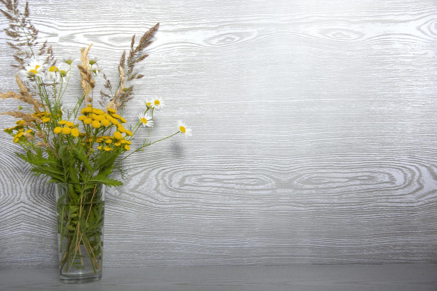 un mazzo di fiori di campo in un vaso di vetro su un tavolo di legno con un posto vuoto per il testo foto