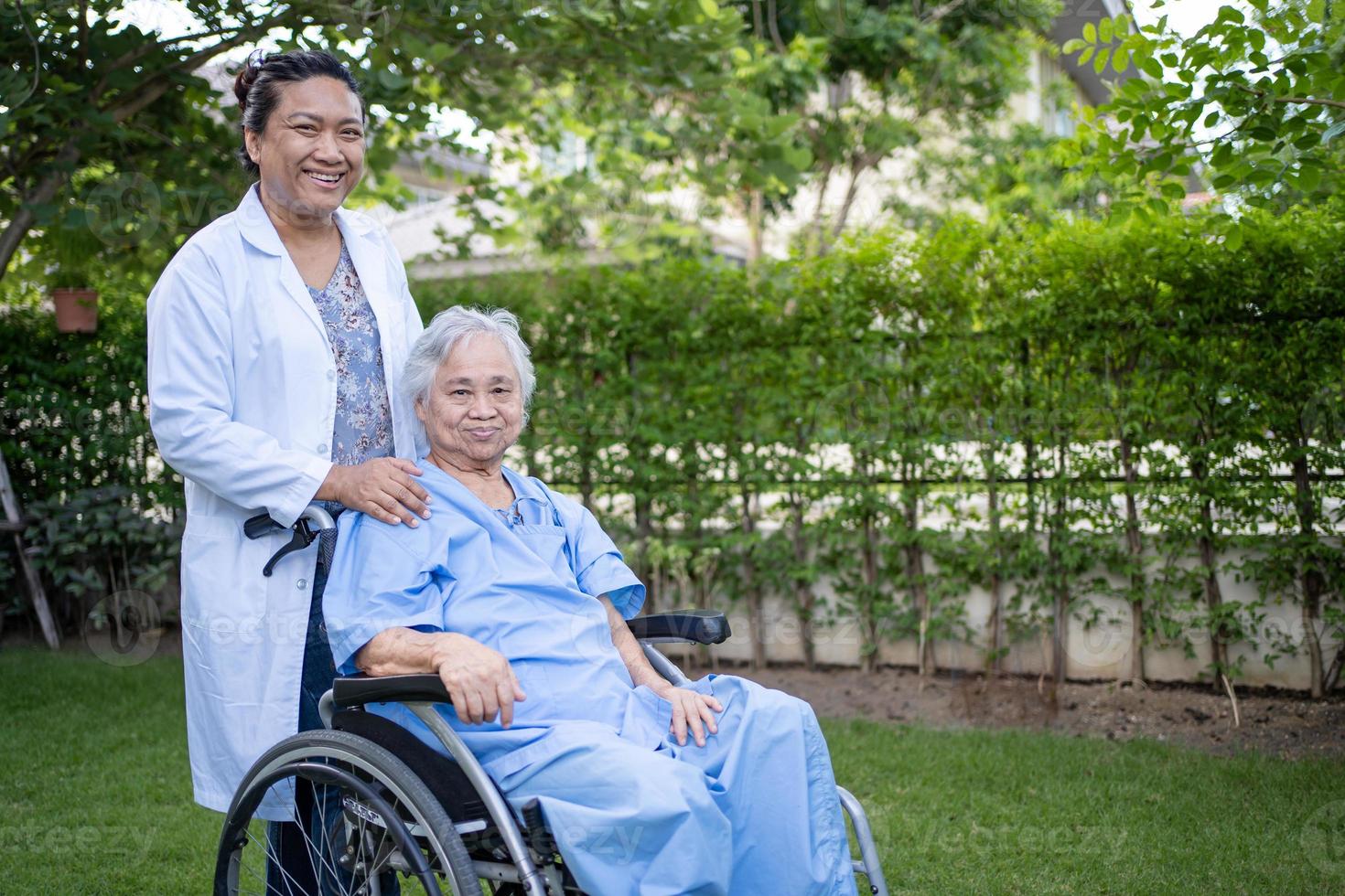 il medico aiuta il paziente asiatico senior della donna che si siede sulla sedia a rotelle al park foto