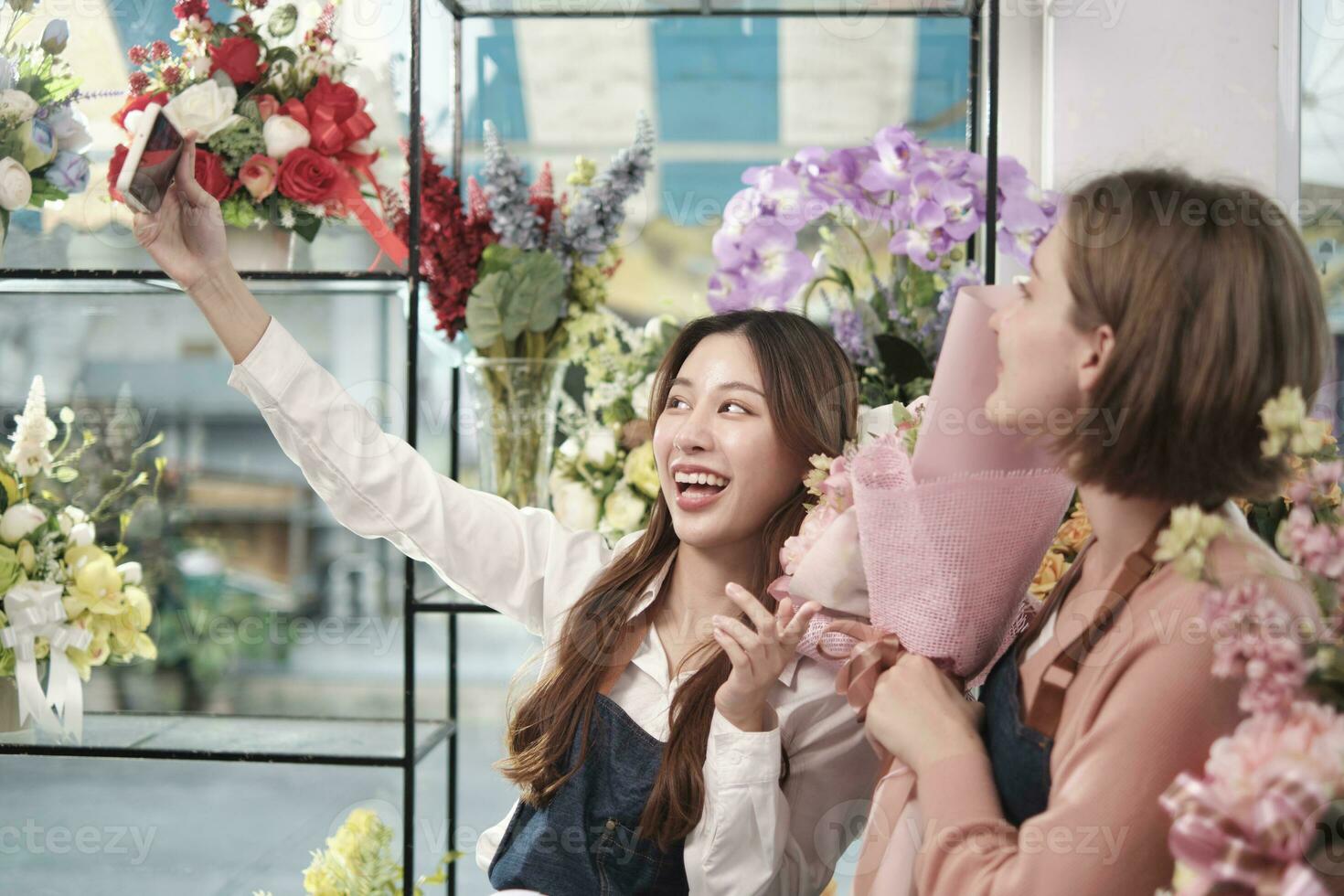 e-commerce attività commerciale compagno, Due giovane femmina fioraio lavoratori mostrare floreale disposizione, in linea vivere streaming, e selfie con smartphone applicazione nel luminosa fiore negozio, bellissimo fiori negozio. foto