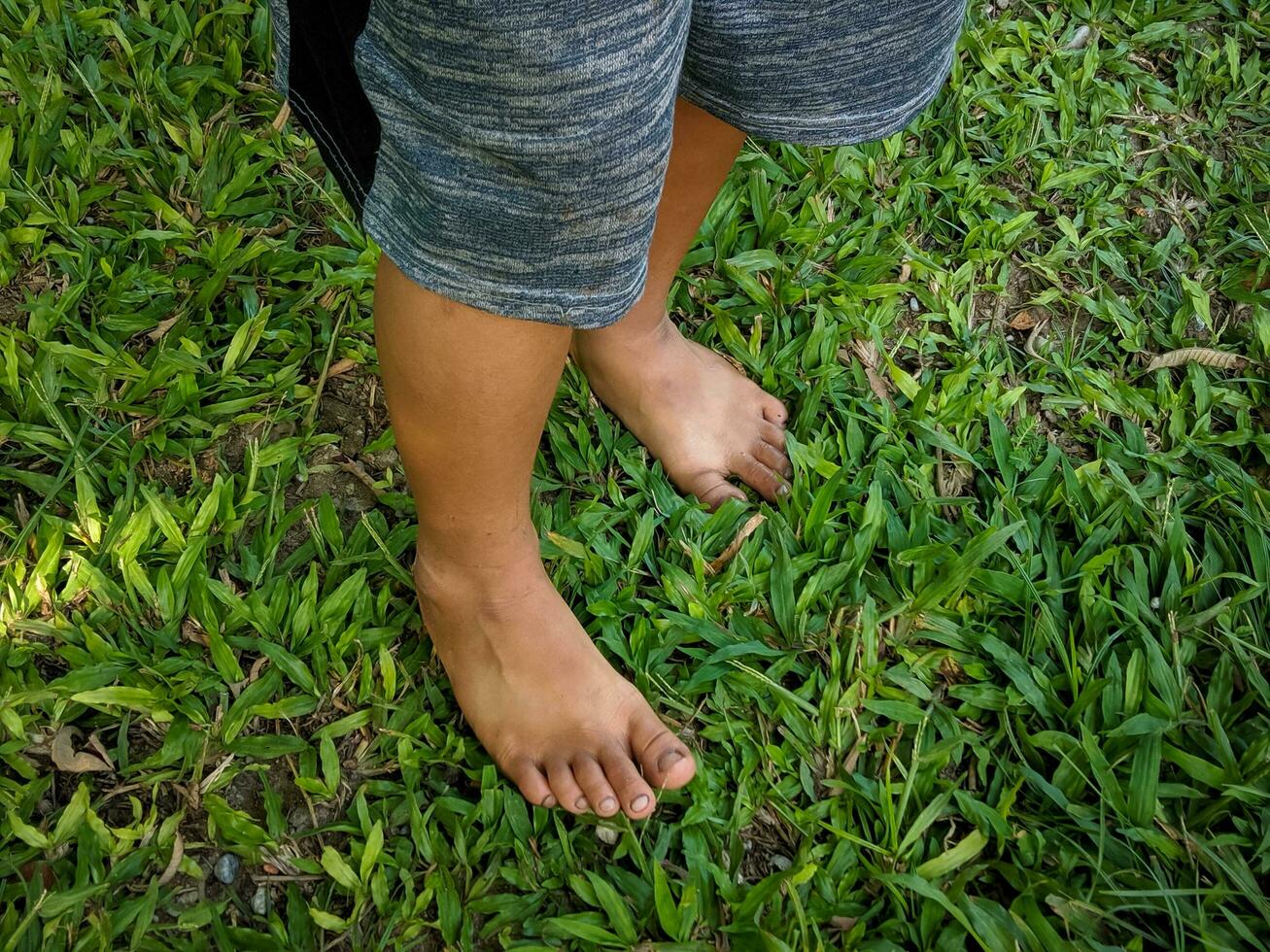 un' poco ragazzo asiatico ragazzo in piedi su il erba a piedi nudi foto