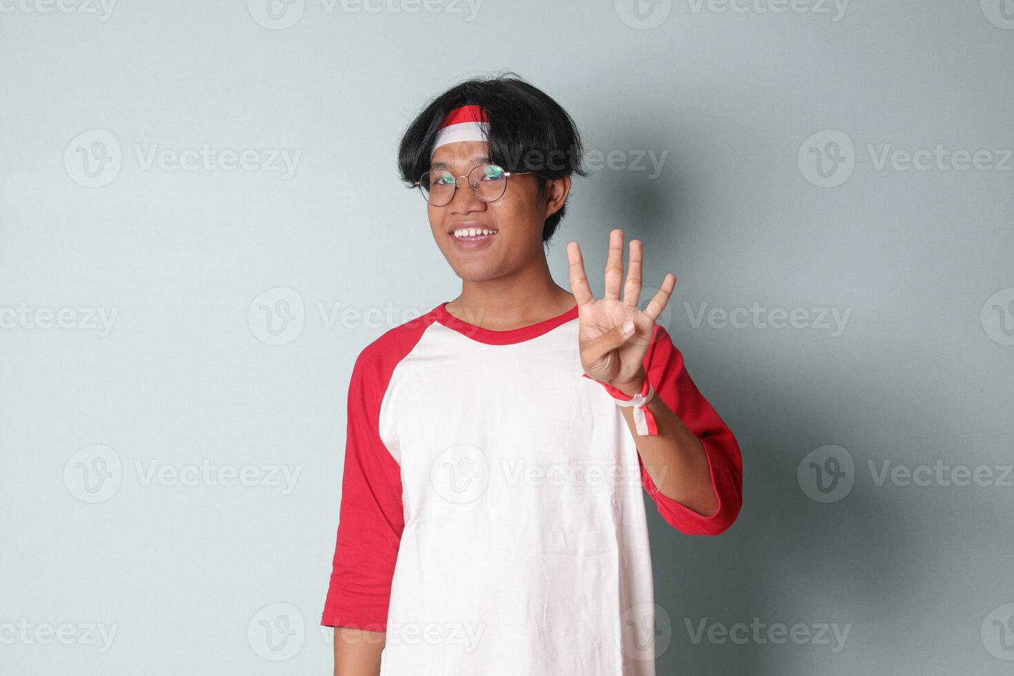 ritratto di attraente asiatico uomo nel maglietta con rosso e bianca nastro su testa, conteggio quattro con dita. isolato Immagine su grigio sfondo foto