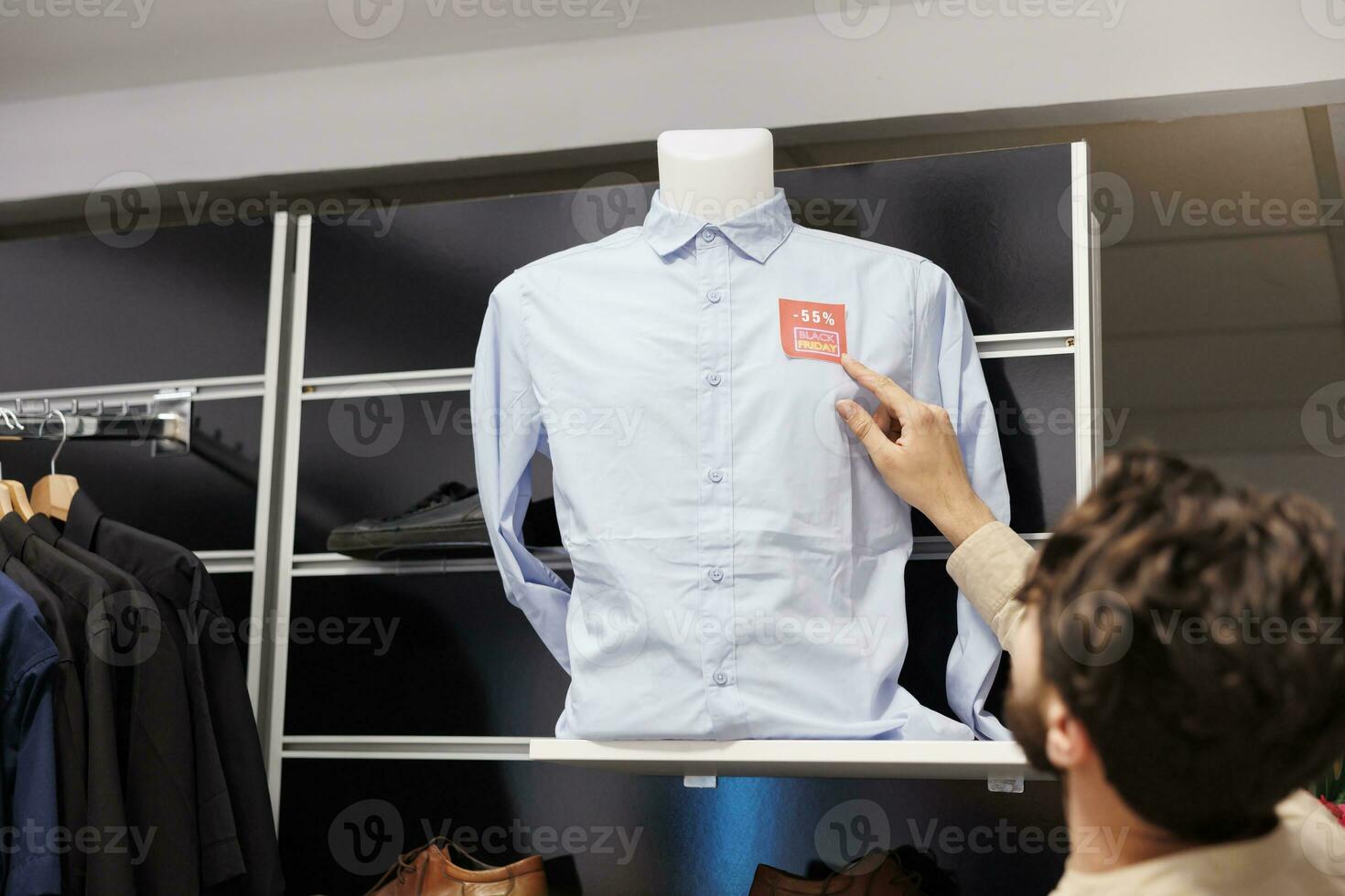 maschio cliente controllo prezzo su camicia mentre in piedi nel capi di abbigliamento negozio, guardare a rosso vendita etichetta etichetta. uomo acquirente conteggio sconto mentre fabbricazione acquisti nel Abiti memorizzare su nero Venerdì foto