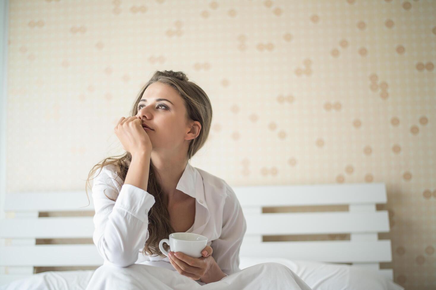 bella donna nella sua camera da letto che beve caffè al mattino foto