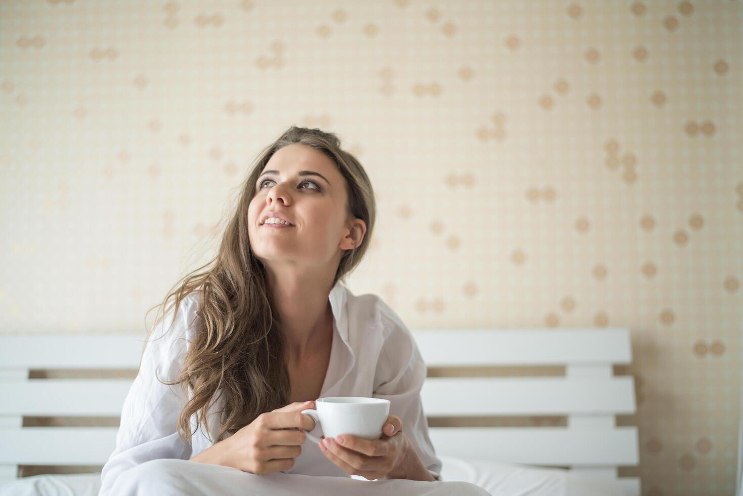 bella donna nella sua camera da letto che beve caffè al mattino foto