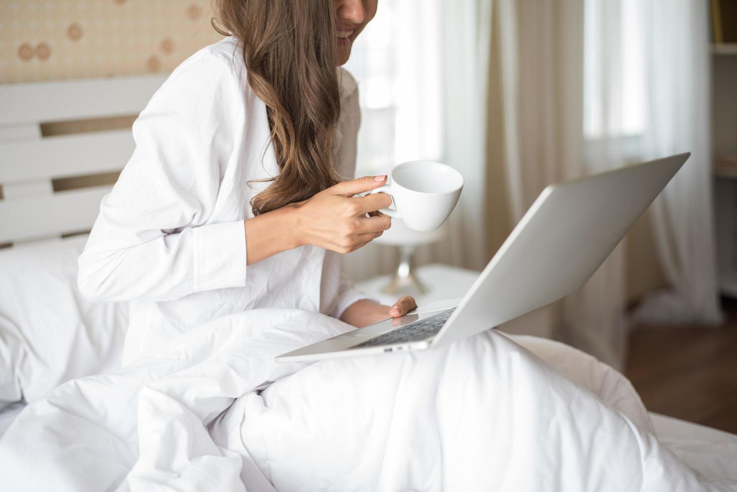 bella donna felice che lavora su un laptop sul letto in casa foto
