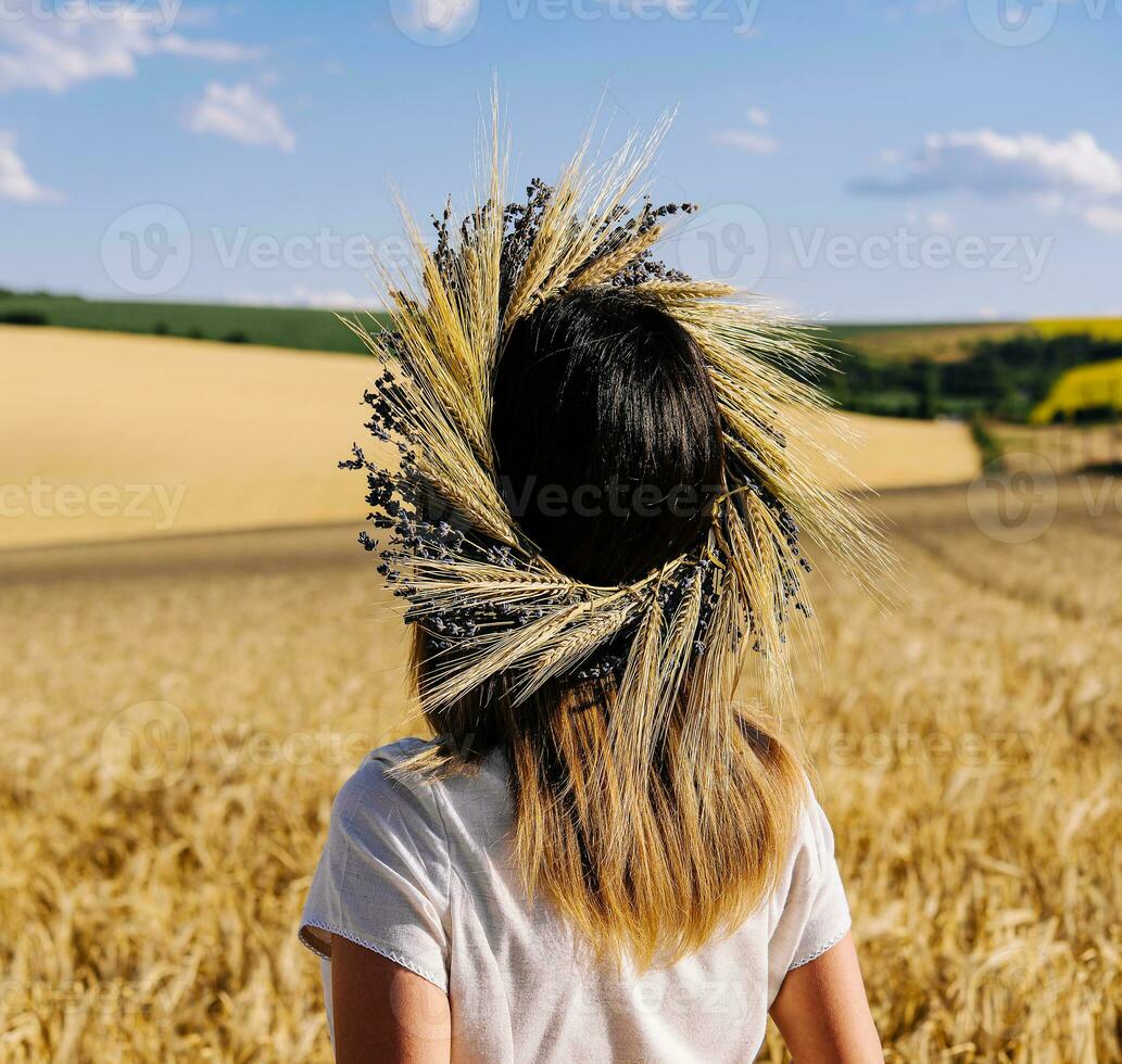 donna nel ghirlanda di fiori con Grano e bianca vestito a piedi lungo cereale campo foto