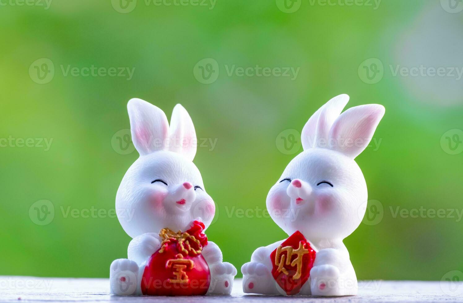 tre carino Cinese coniglietti Bambola Tenere un' rosso i soldi Borsa e Sorridi con verde natura sfocato sfondo. bello coniglio personaggio disegni per medio autunno Festival, anno di il coniglio 2023, e Pasqua foto