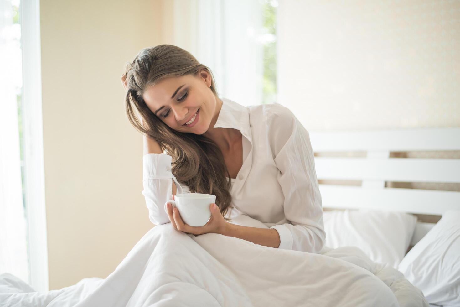 bella donna nella sua camera da letto che beve caffè al mattino foto