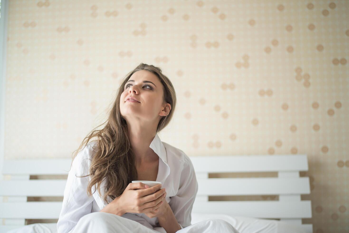 bella donna nella sua camera da letto che beve caffè al mattino foto