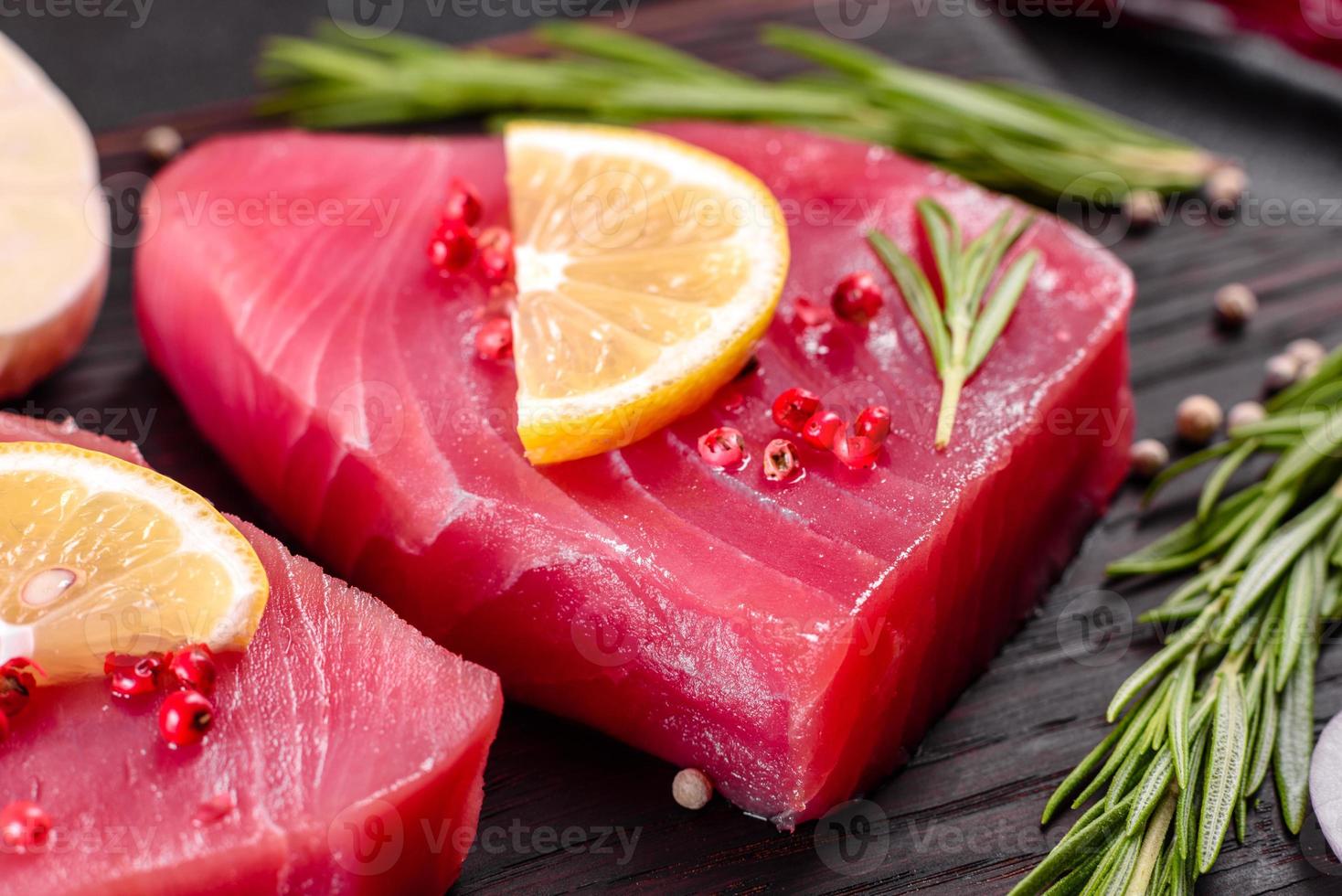 Bistecche di filetto di tonno fresco con spezie ed erbe aromatiche su sfondo nero foto