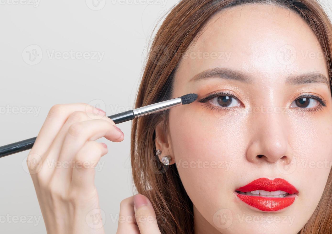 ritratto bella donna asiatica con pennello per gli occhi trucco su sfondo bianco foto
