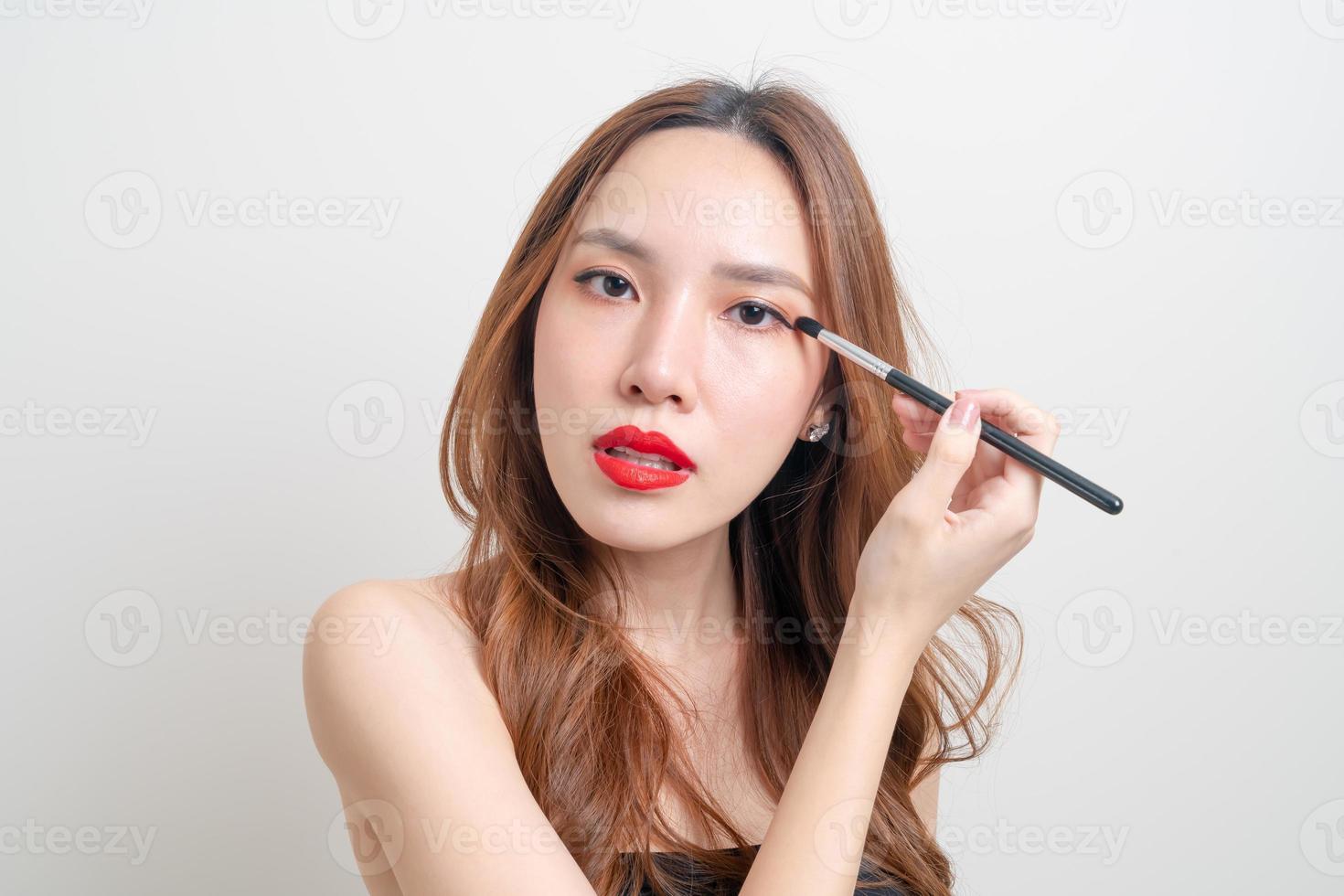 ritratto bella donna asiatica con pennello per gli occhi trucco su sfondo bianco foto