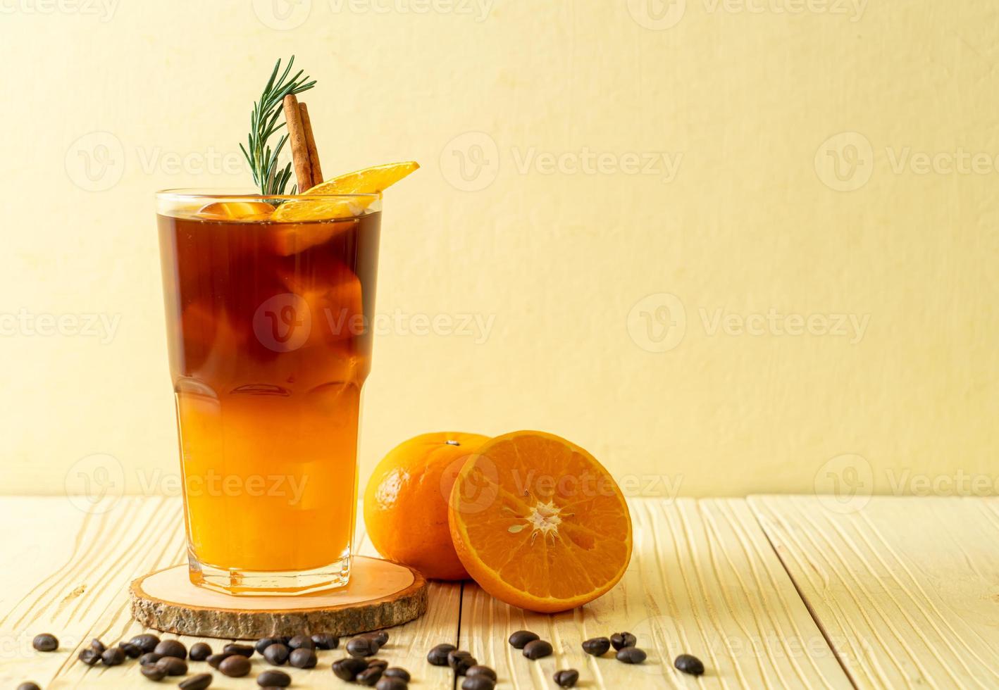 un bicchiere di caffè nero americano ghiacciato e uno strato di succo di arancia e limone decorato con rosmarino e cannella foto