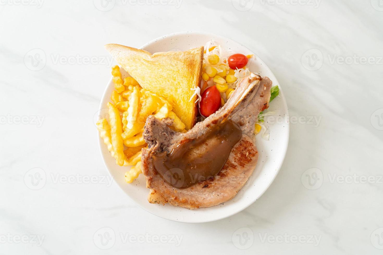 bistecca di braciola di maiale con patatine e mini insalata su piatto bianco foto