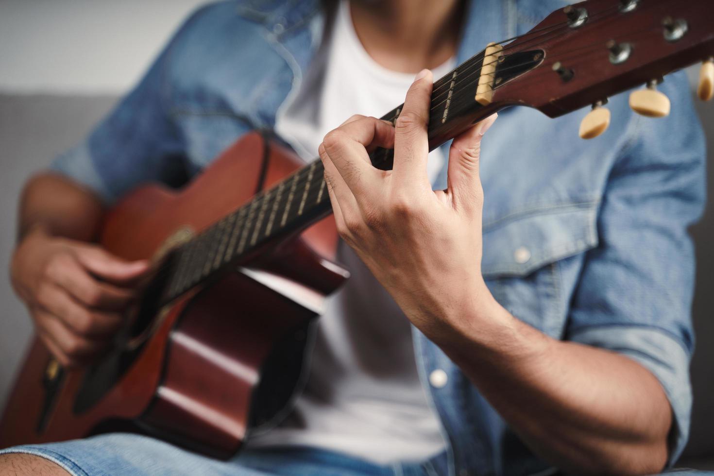 goditi l'uomo che si esercita o suona la chitarra sul divano del soggiorno foto