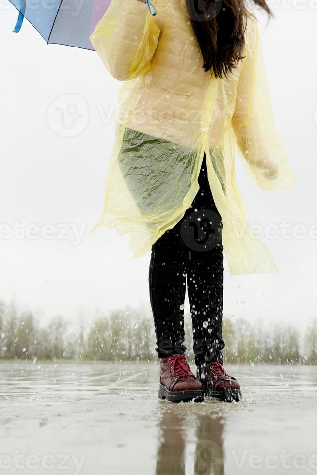 donna che gioca sotto la pioggia, salta nelle pozzanghere con schizzi foto