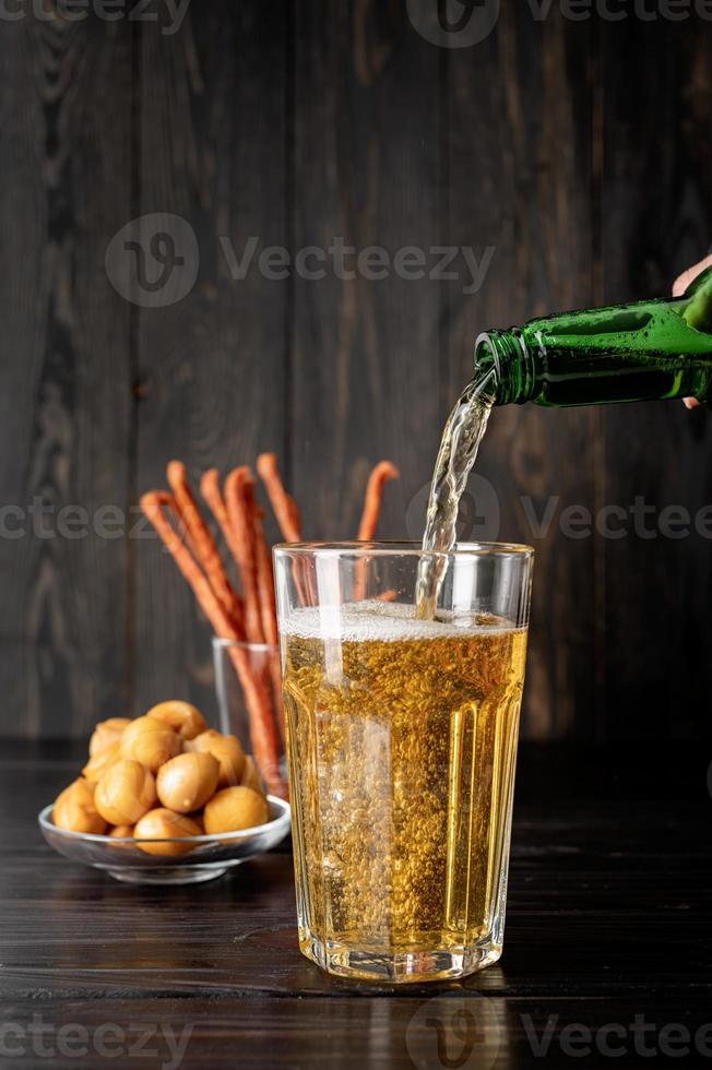 birra che versa dalla bottiglia in vetro, fondo di legno nero foto