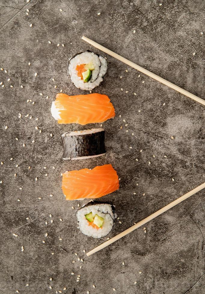 rotoli di sushi posizionati tra le bacchette su sfondo scuro foto