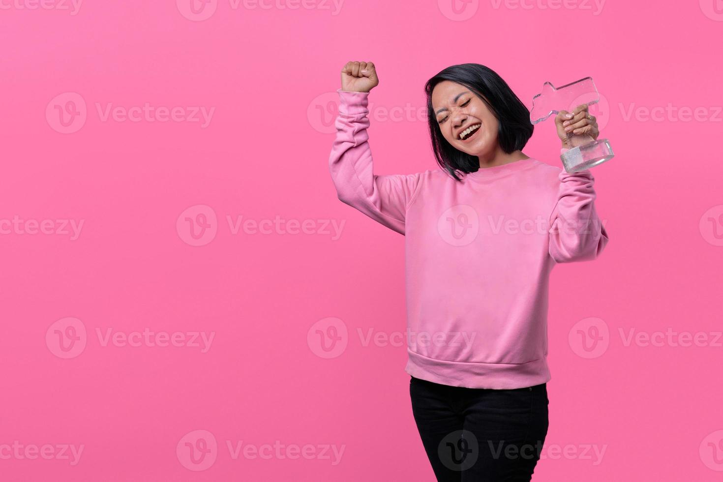 la donna che tiene la statua del premio riceve una piacevole sorpresa e alza la mano foto