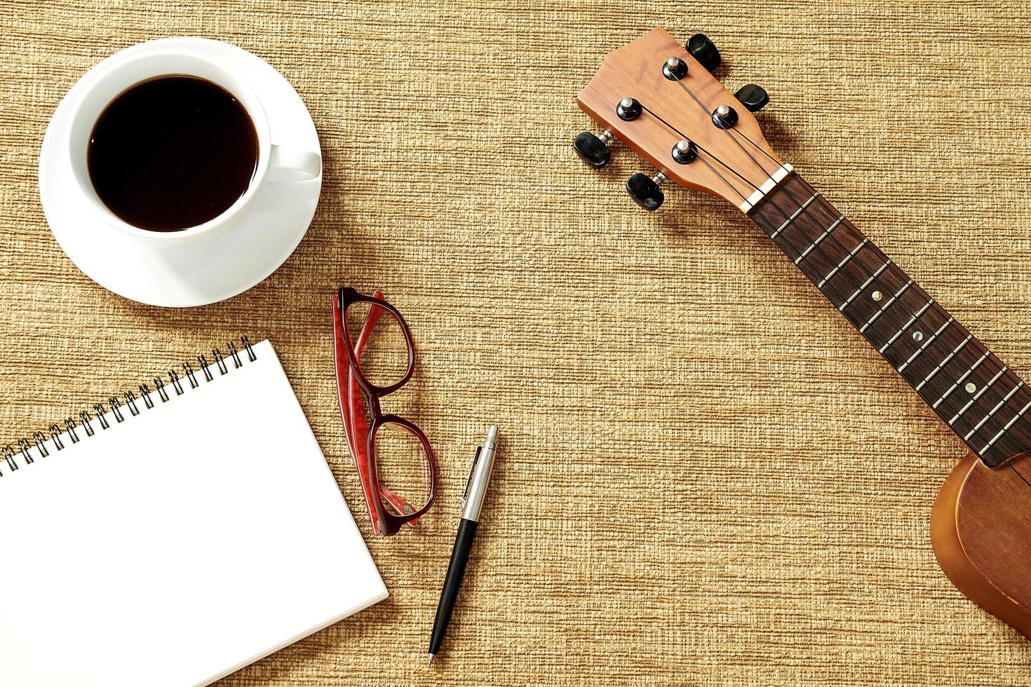vista dall'alto di ukulele, taccuino, penna, tazza da caffè e bicchieri foto