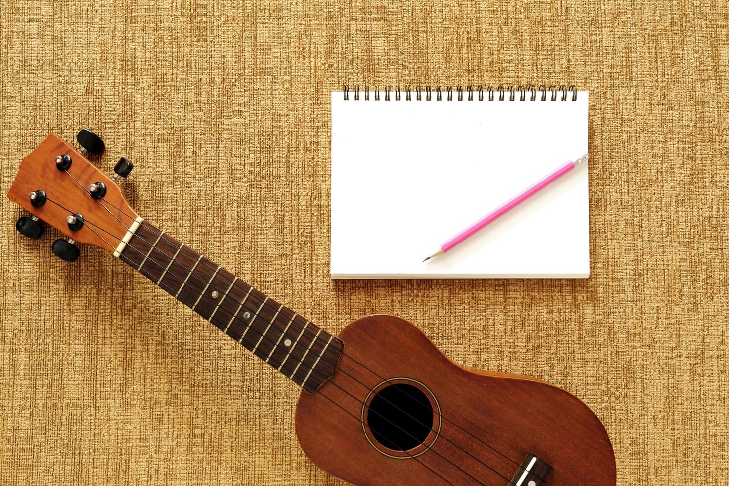 vista dall'alto di ukulele con taccuino e matita posizionati su favoloso marrone foto