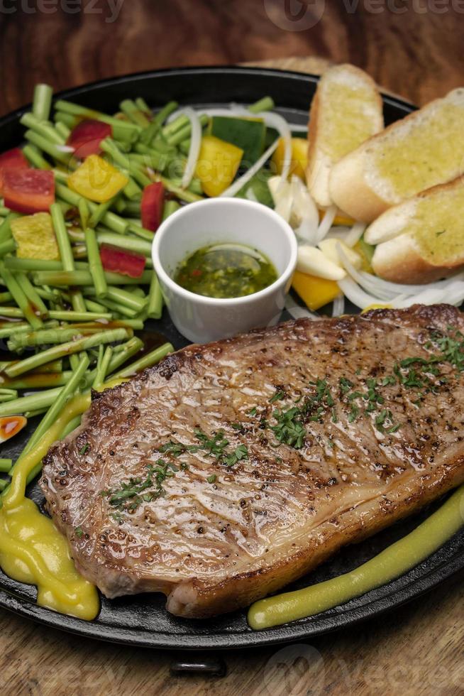 Bistecca di filetto di manzo biologico sfrigolante su piatto caldo con verdure miste e salsa chimichurri foto