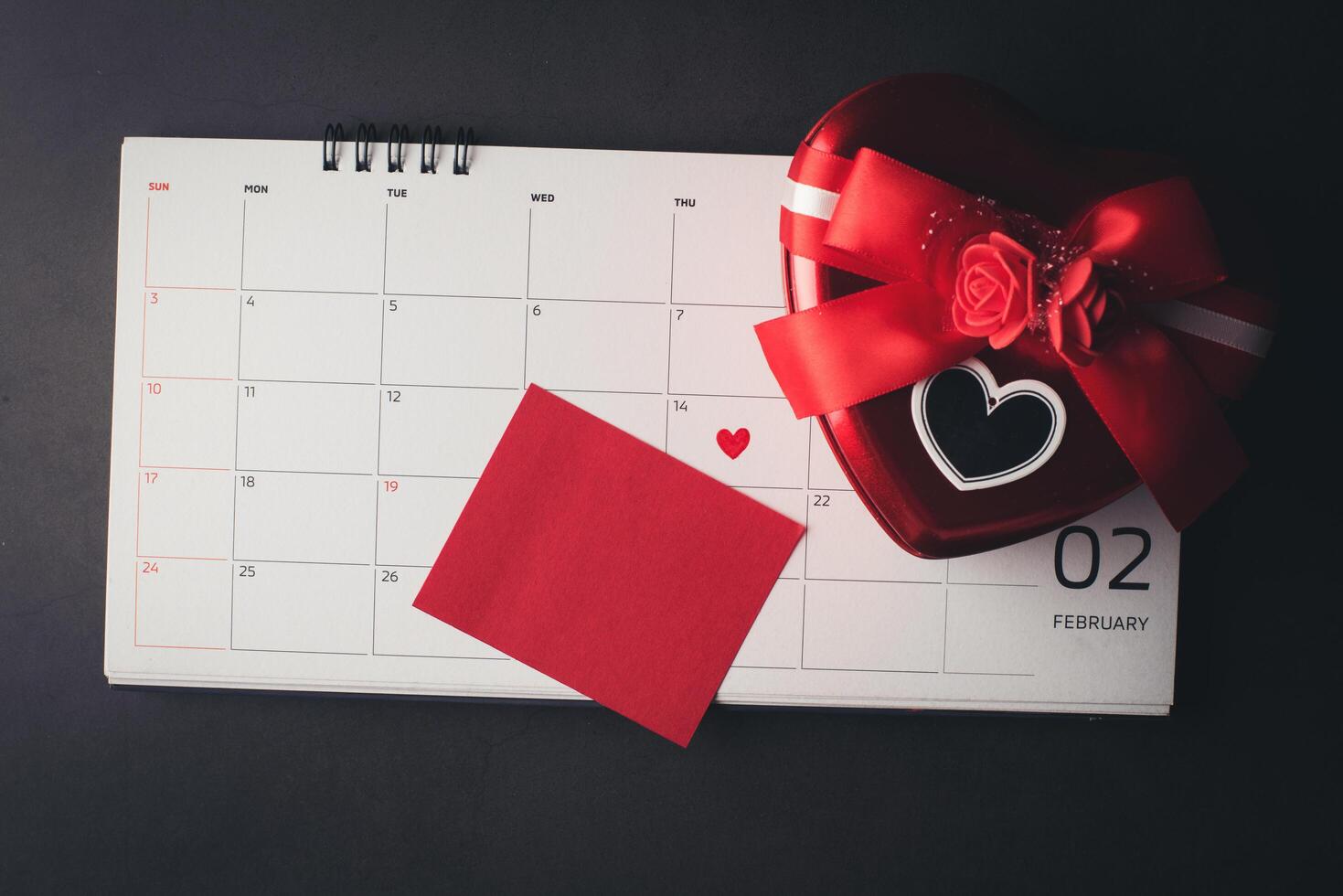 cuore rosso il 14 febbraio sul calendario con confezione regalo a forma di cuore. foto